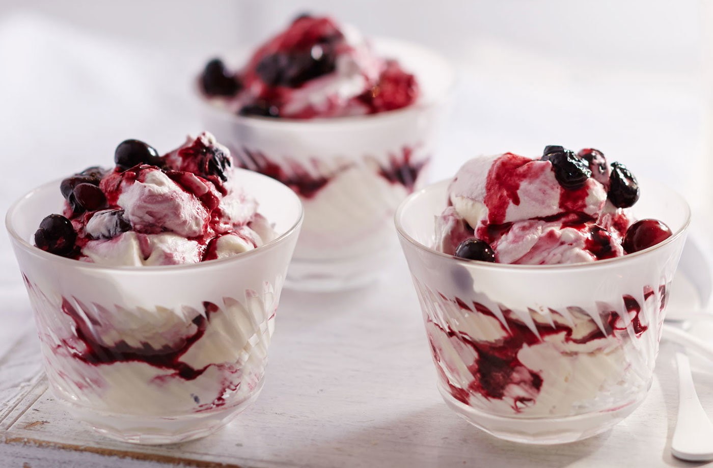 A Summer Berry Fool in a tall glass. The dish features multiple fresh berries layered with whipped cream. 